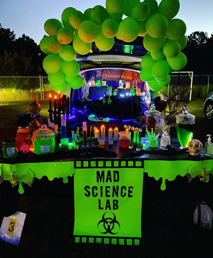 a table topped with lots of green balloons next to a sign that says mad science lab