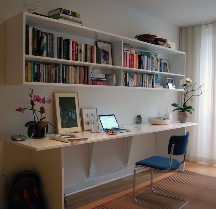 a desk with a laptop and bookshelf in front of a window filled with flowers