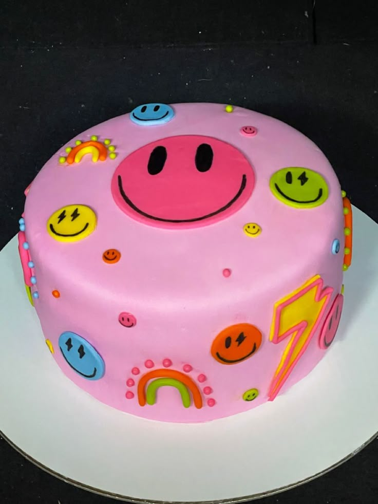 a pink cake decorated with smiley faces and other decorations on a white plate in front of a black background