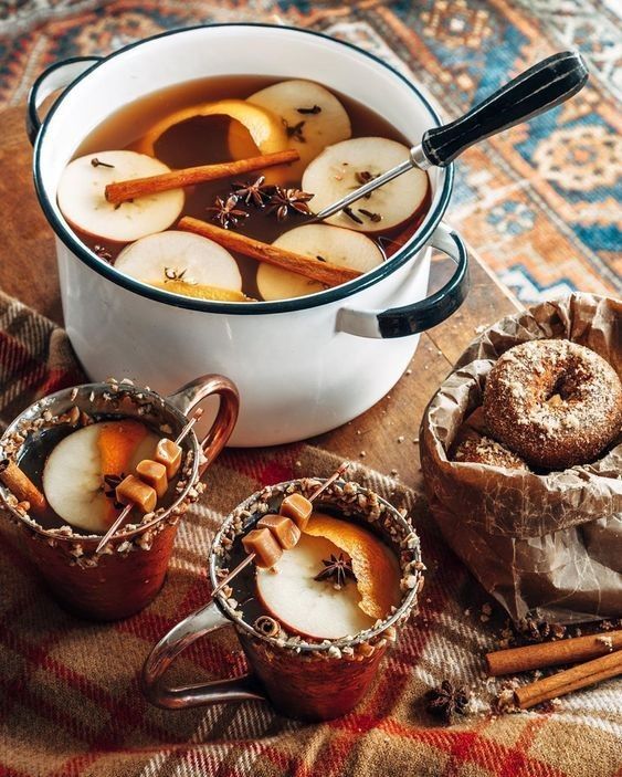 apples and cinnamon are being served in the bowl with two mugs next to them