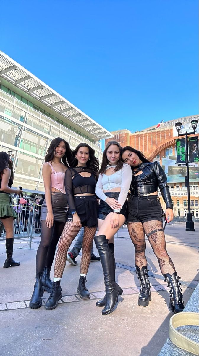 four girls are posing for the camera in front of a building and some people standing around