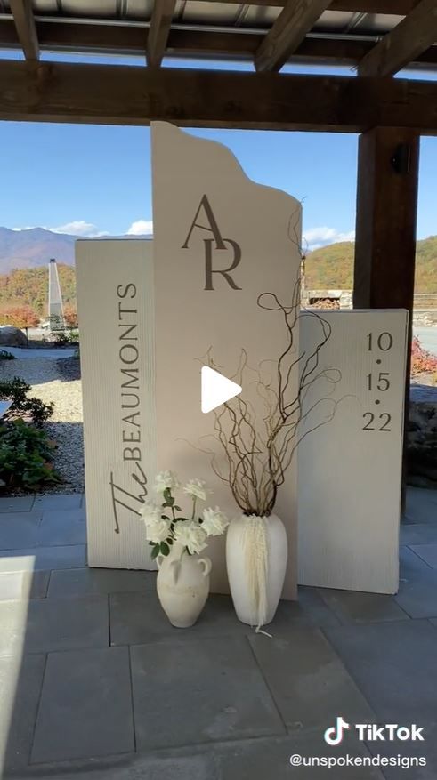 two white vases with flowers are sitting on the ground in front of a sign