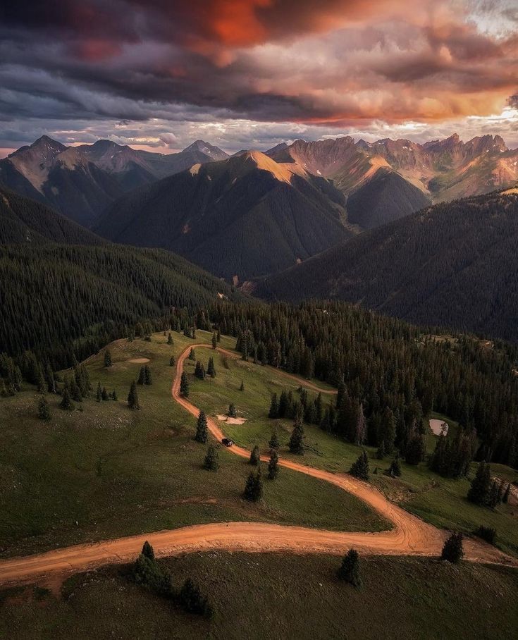 an aerial view of a dirt road in the middle of mountains under a cloudy sky