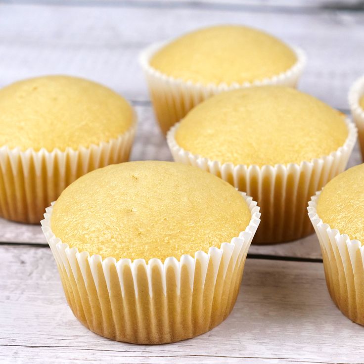 six yellow cupcakes sitting on top of a wooden table