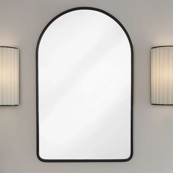 an arched mirror mounted on the wall next to two lamps and a lamp shade in front of it