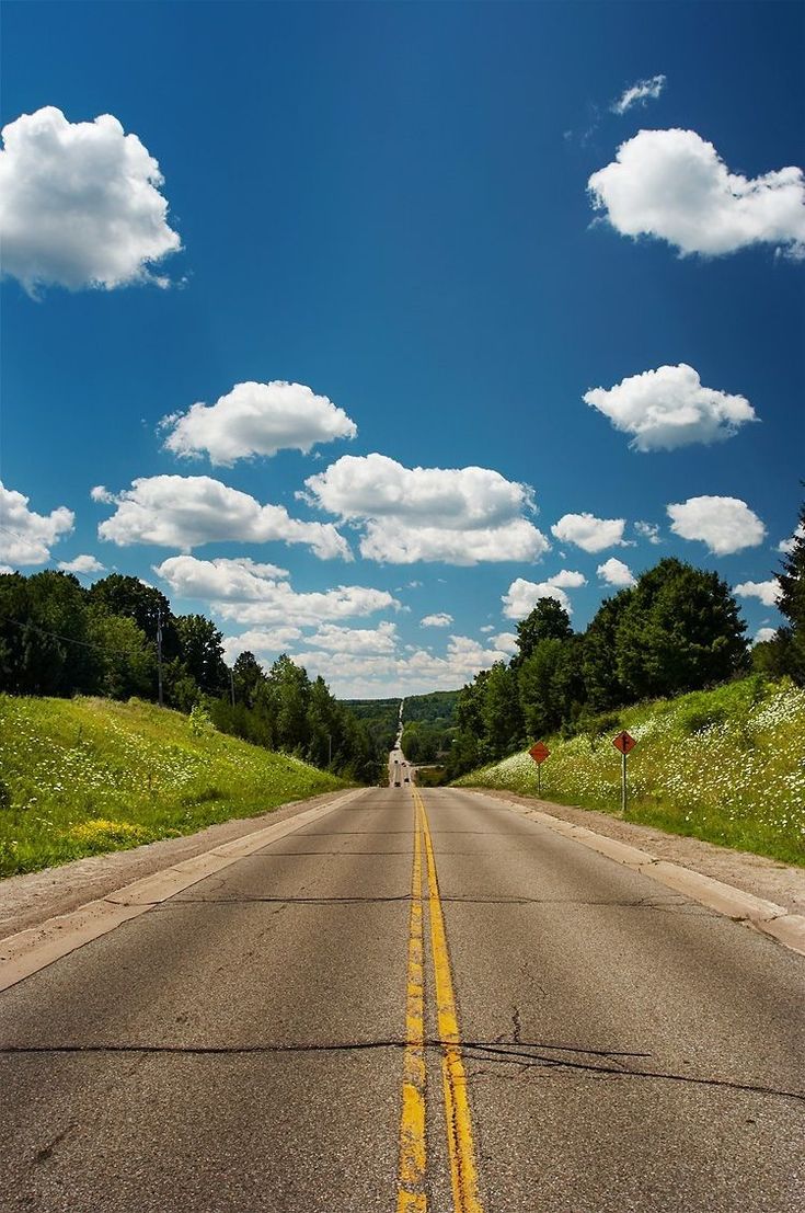 a van driving down the middle of a road under a blue sky with white clouds