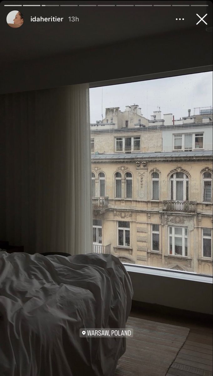 a bed sitting in front of a window next to a tall building