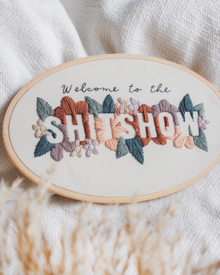 embroidered sign that says, welcome to the shitshow with flowers and leaves on it