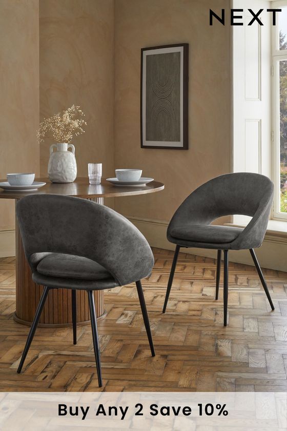 two grey chairs sitting on top of a wooden floor next to a table with plates and cups