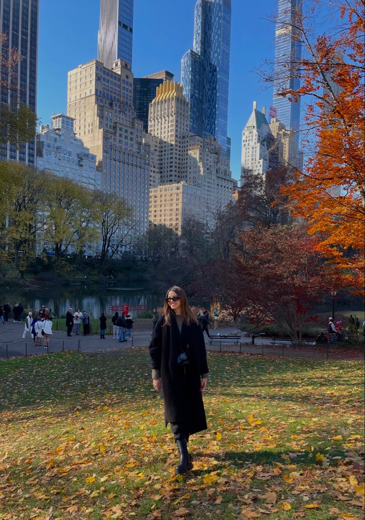 a woman standing on top of a grass covered field in front of tall skyscrapers