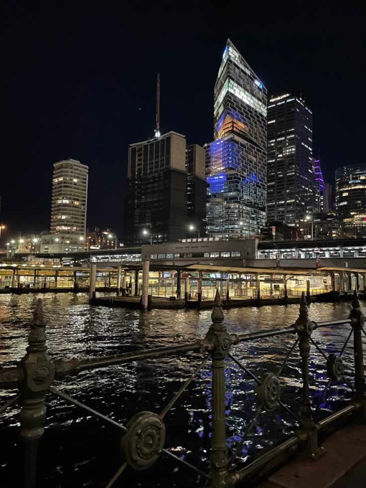 the city skyline is lit up at night, with lights reflecting in the water and buildings on either side