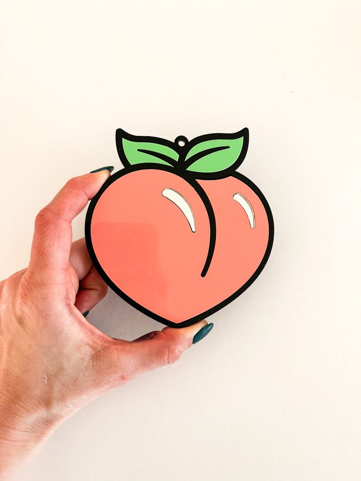 a hand holding up a sticker with a peach on it