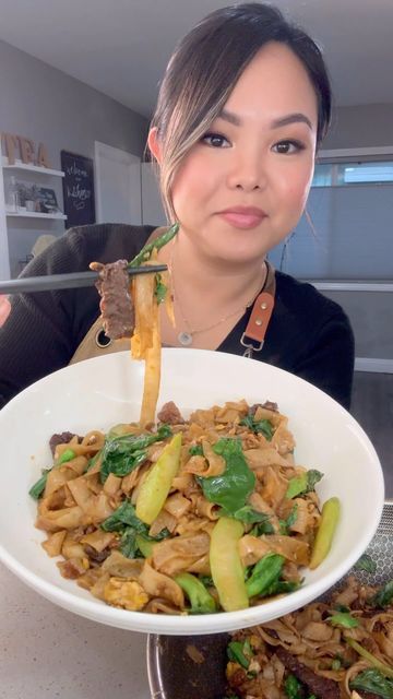 a woman is holding a plate of food with chopsticks sticking out of it