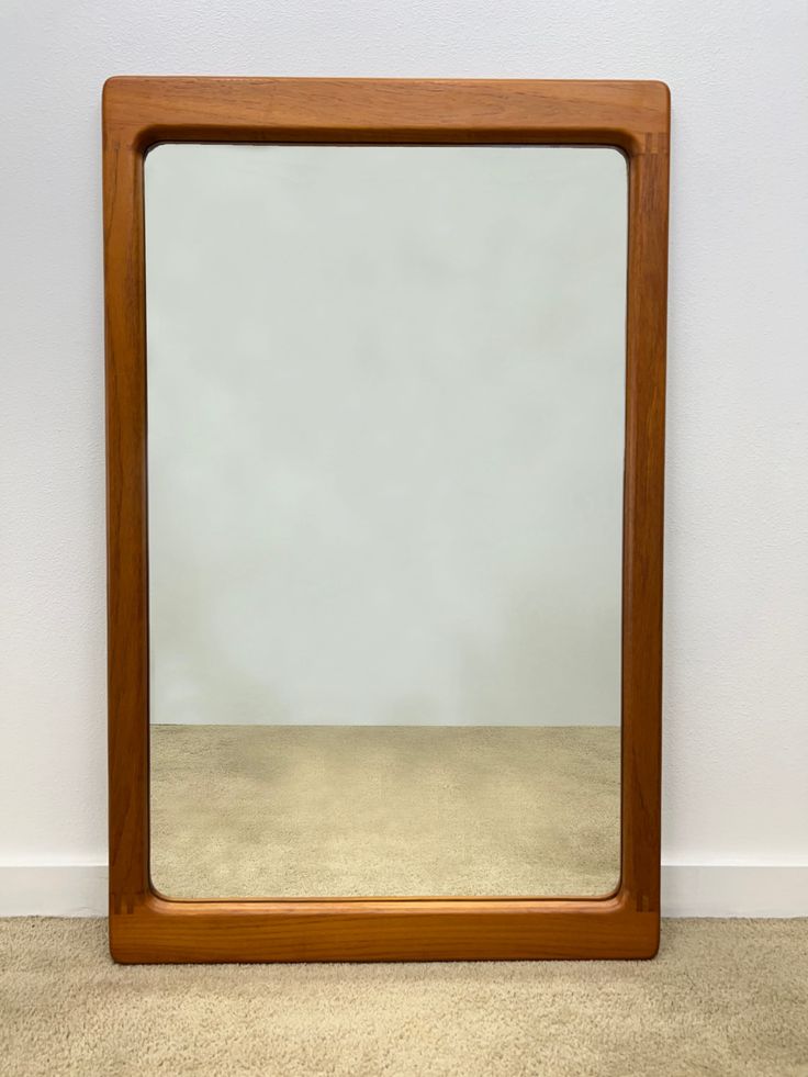 a mirror sitting on top of a floor next to a white wall with a brown frame