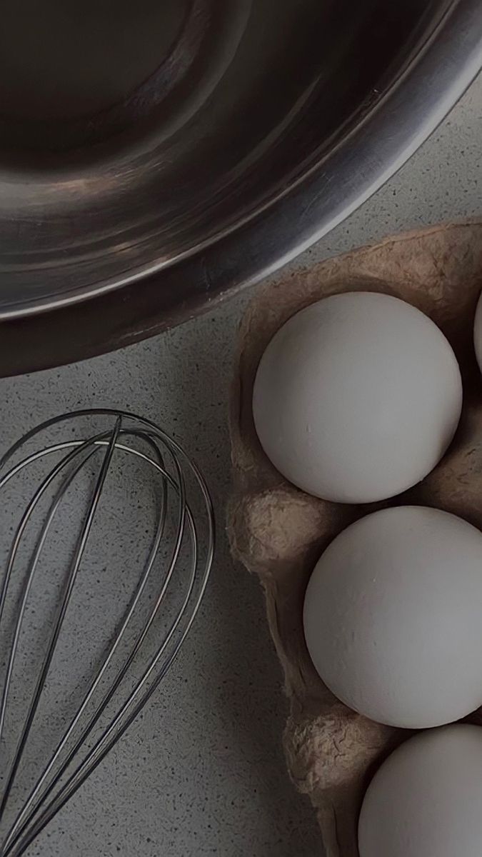 six eggs in an egg carton next to a whisk