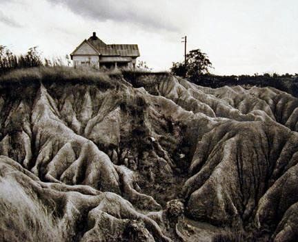 black and white photograph of an old house on top of a hill with rocks in the foreground