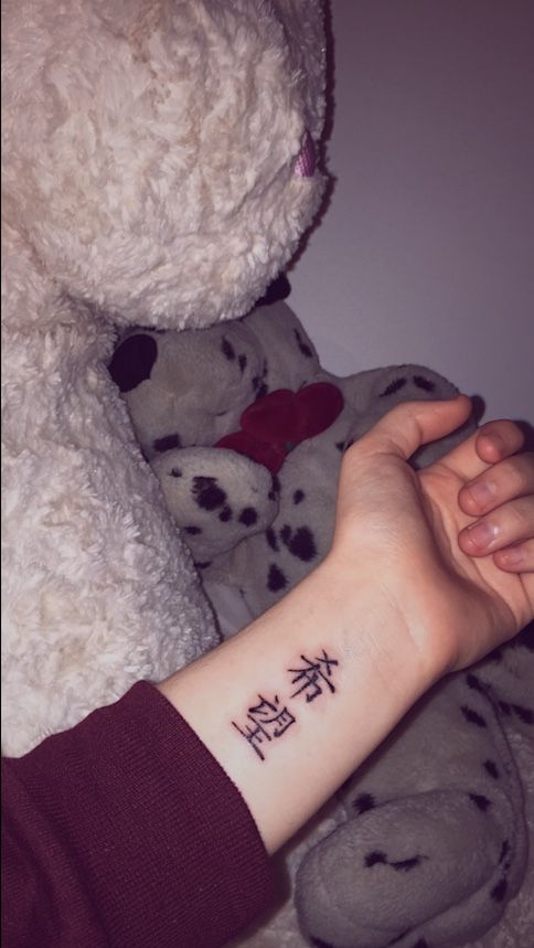 a person with a tattoo on their arm holding a teddy bear in front of them