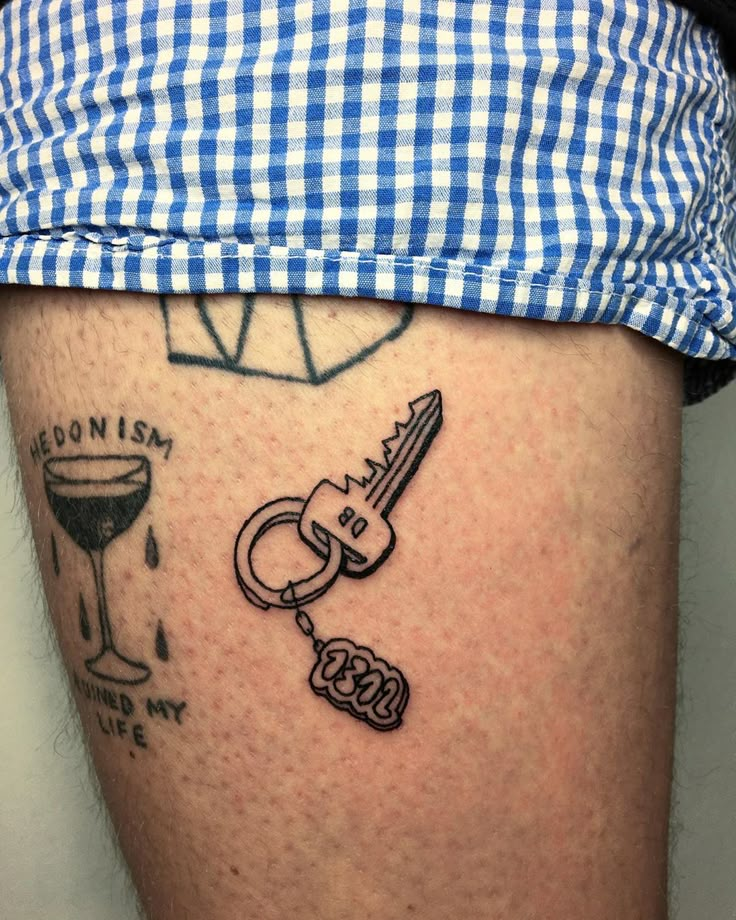 a person with a tattoo on their leg has a key and wine glass attached to it