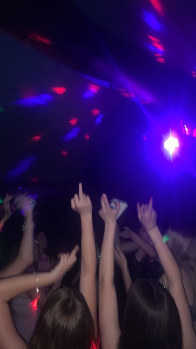 several people are dancing at a party with their hands in the air and lights on