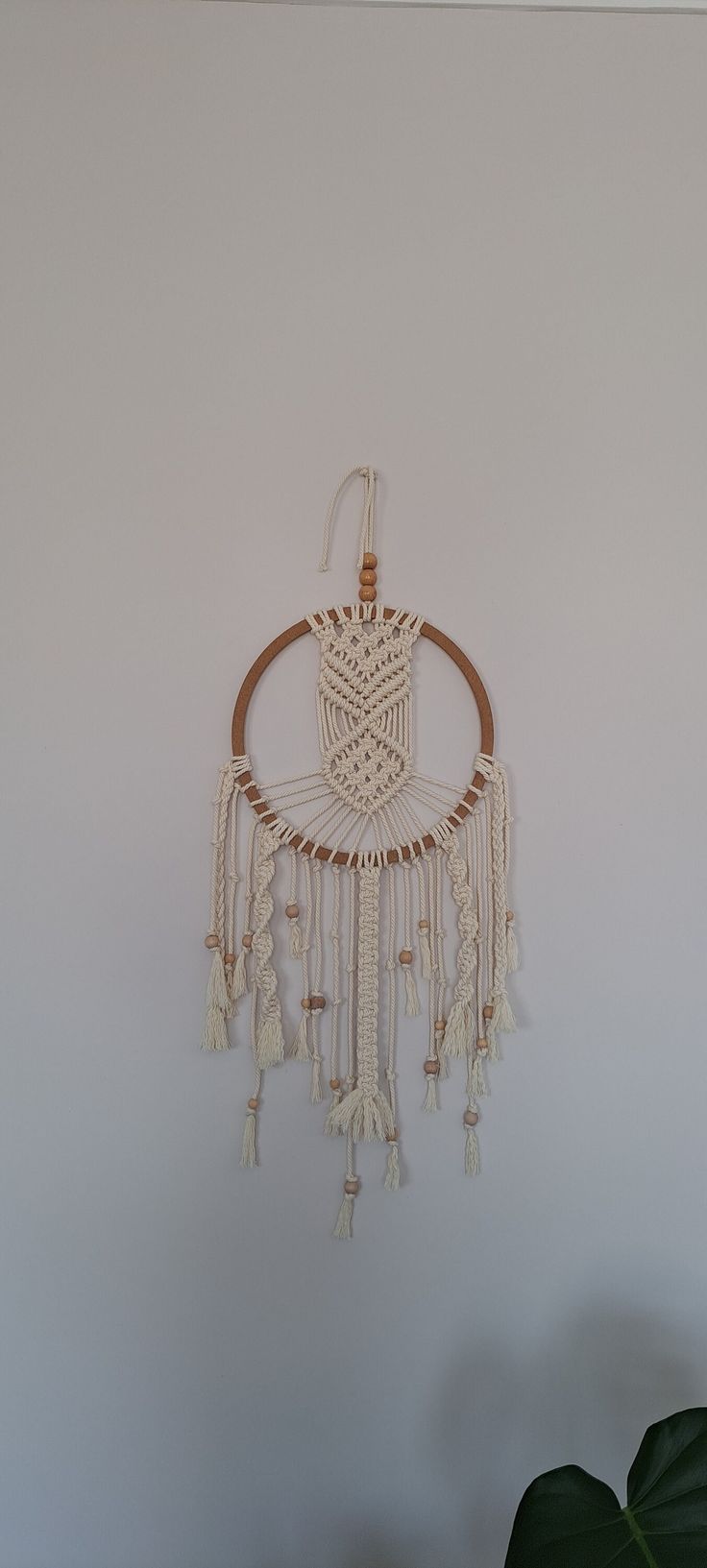 a white wall hanging with some tassels on it's sides and a plant in the corner