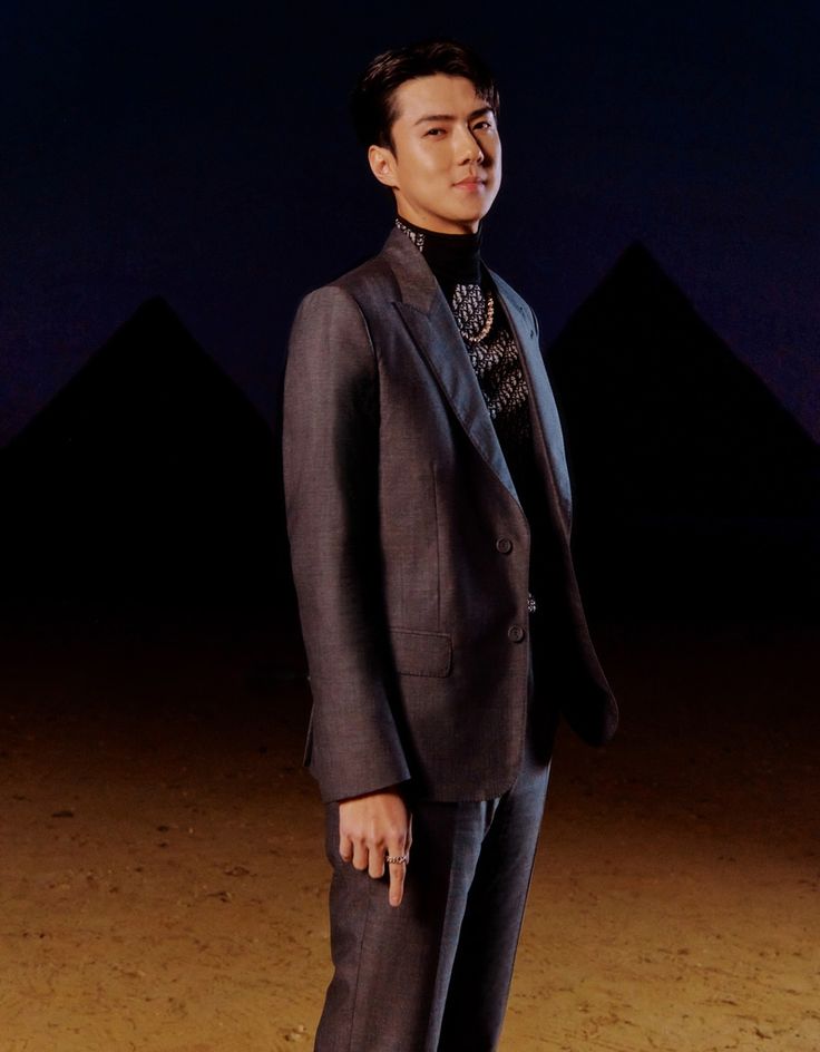 a man standing in front of the pyramids wearing a suit and tie with his hand on his hip