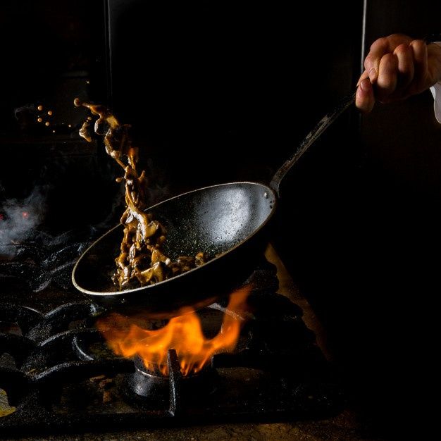 a person is cooking food in a wok on the stove with flames coming from it