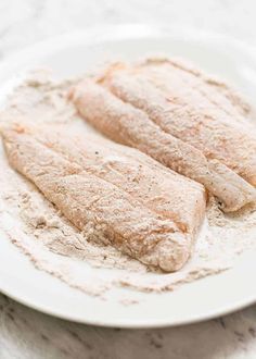 two fish fillets on a white plate covered in powdered sugar sitting on a marble surface