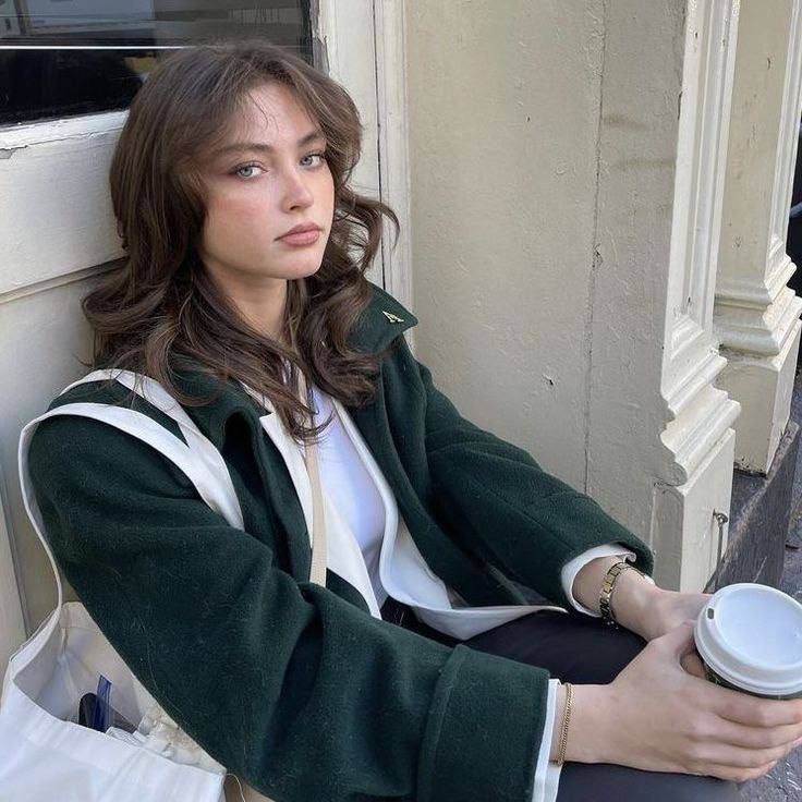 a woman sitting on the side of a building with her arms crossed and looking off into the distance