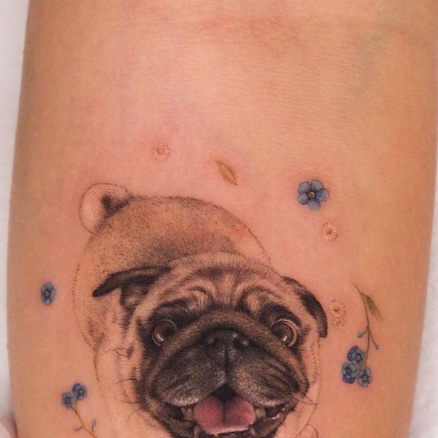 a small pug dog tattoo on the right side of the leg with blue flowers around it