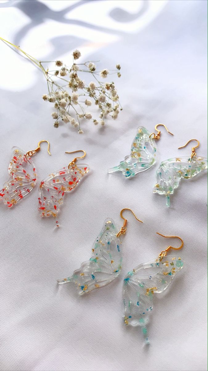 four different types of earrings on a white tablecloth with flowers and leaves in the background