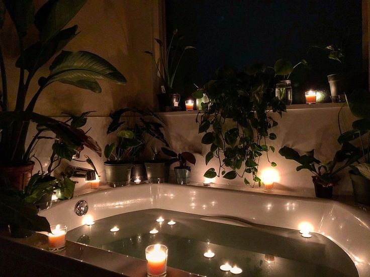 candles are lit in the bathtub surrounded by potted plants