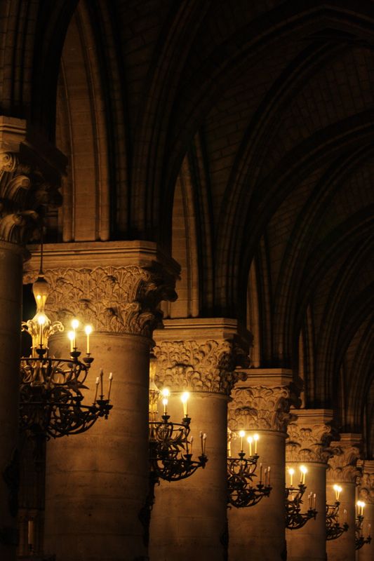 candles are lit in the middle of an old building with columns and arches on both sides