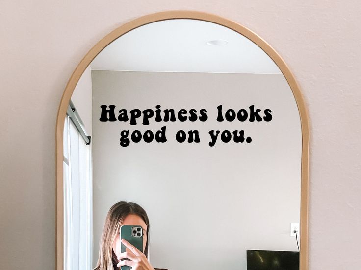 a woman taking a selfie in front of a mirror that says happiness looks good on you