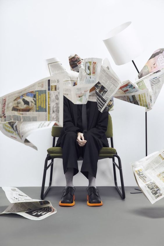 a man sitting in a chair surrounded by papers and reading glasses, with his head turned to the side