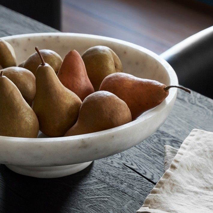 a white bowl filled with pears on top of a wooden table next to a napkin