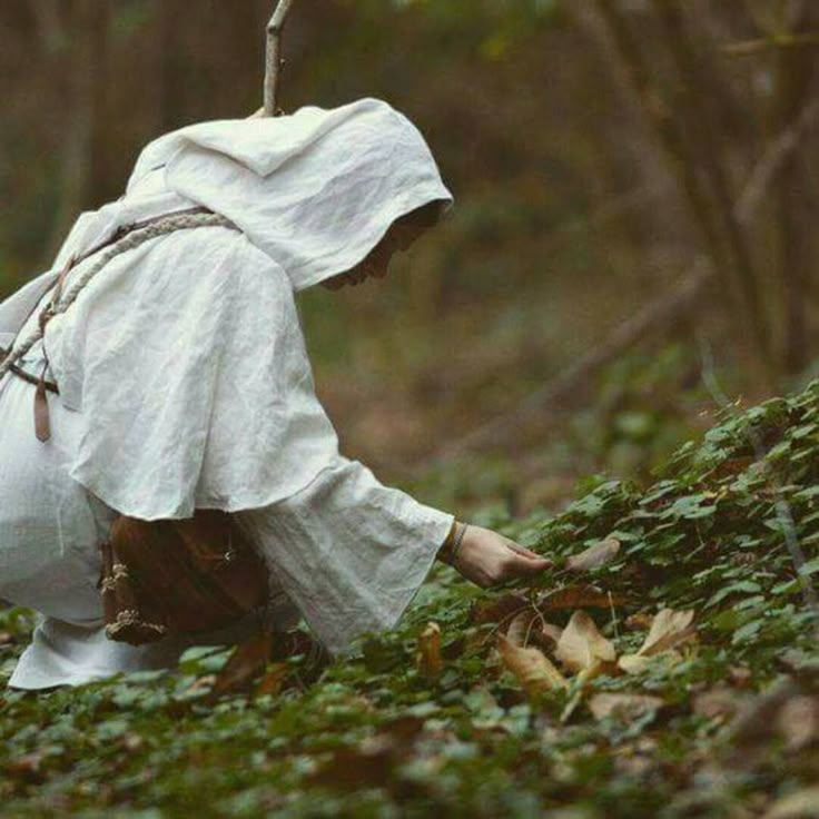 a person dressed in white picking leaves from the ground