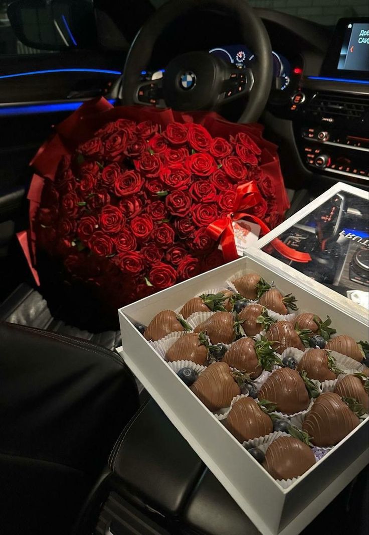 two boxes of chocolate covered strawberries and roses in front of a car steering wheel