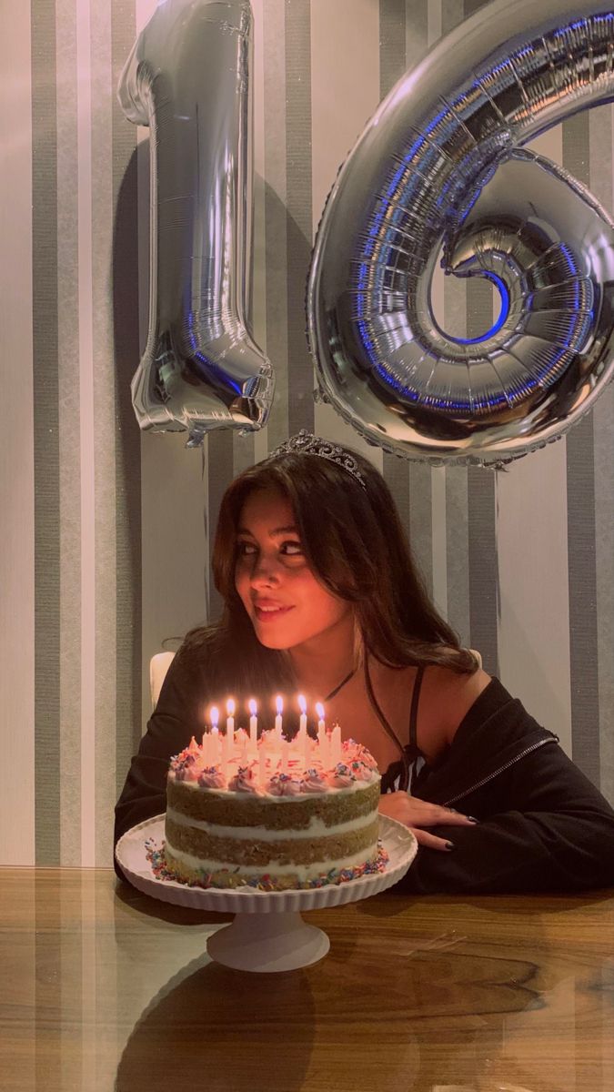 a woman sitting in front of a birthday cake with candles on it and the number six behind her