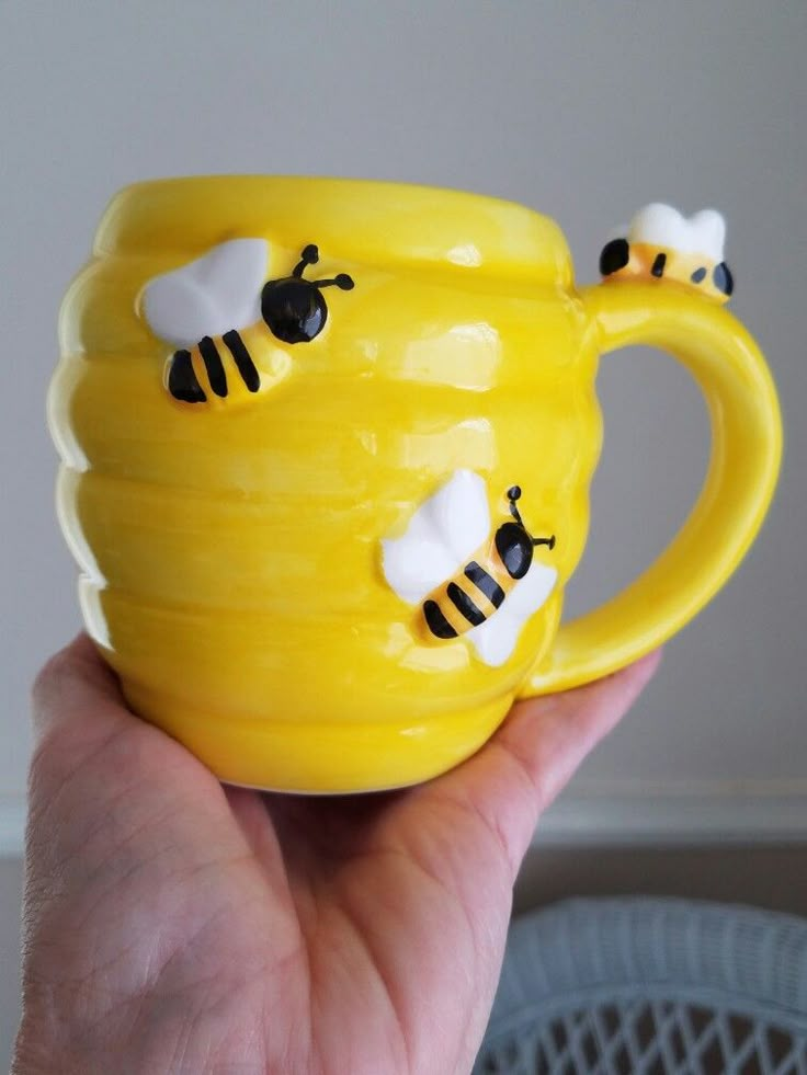 a hand holding a yellow mug with bees on it