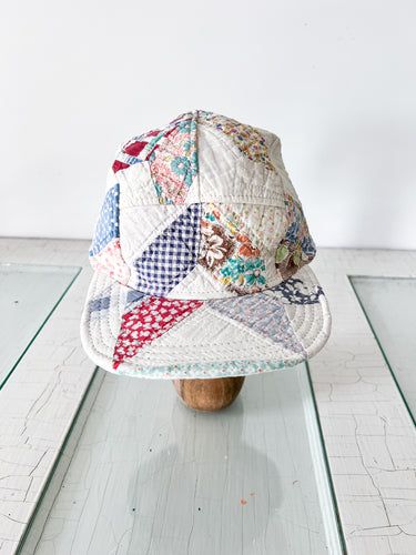 a hat that is sitting on top of a wooden headpiece with a patchwork pattern