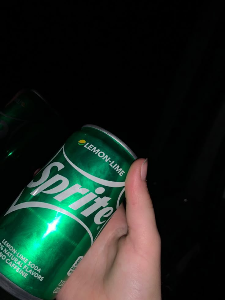 a can of sprite beer being held by someone's hand in the dark