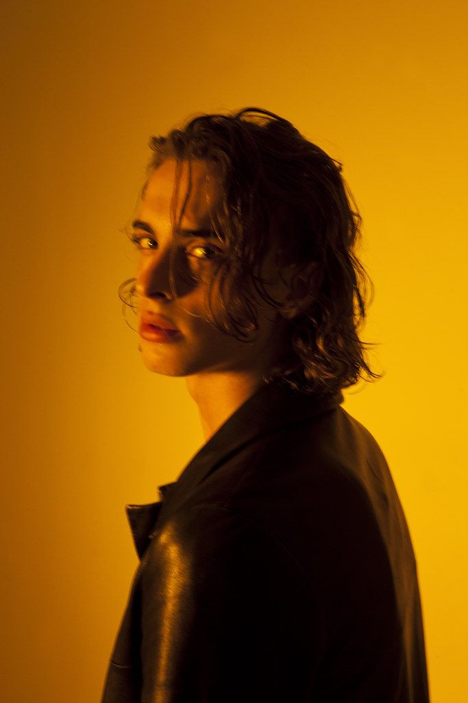 a woman with curly hair wearing a black shirt and looking off to the side in front of a yellow background