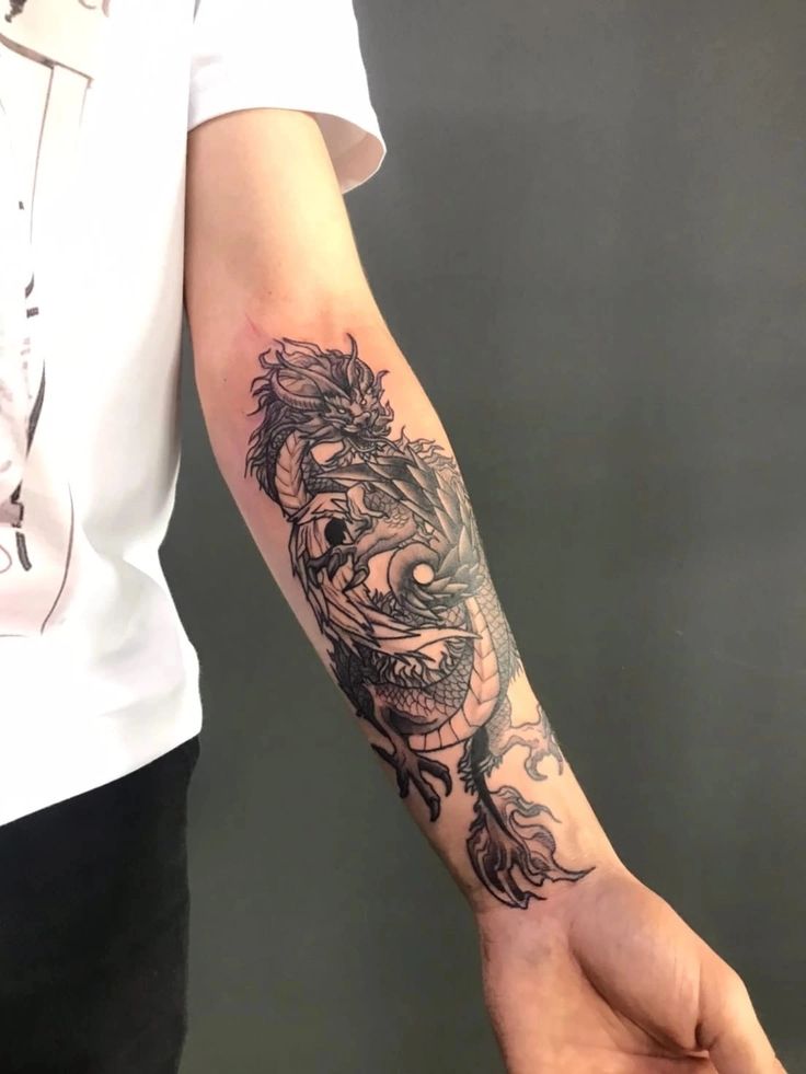 a person holding their arm with a dragon tattoo on it's left forearm and wrist