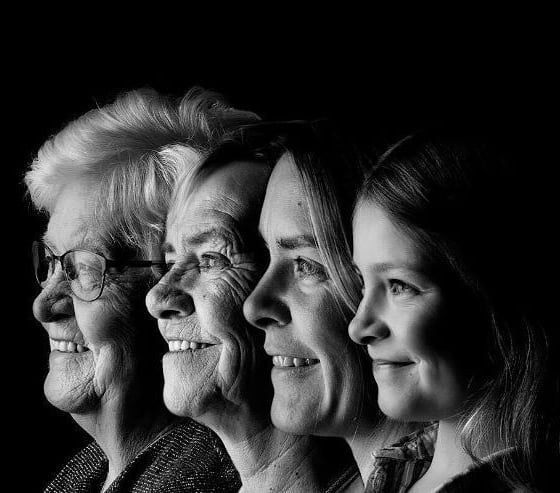 black and white photograph of four women smiling at the camera with their heads tilted to the side