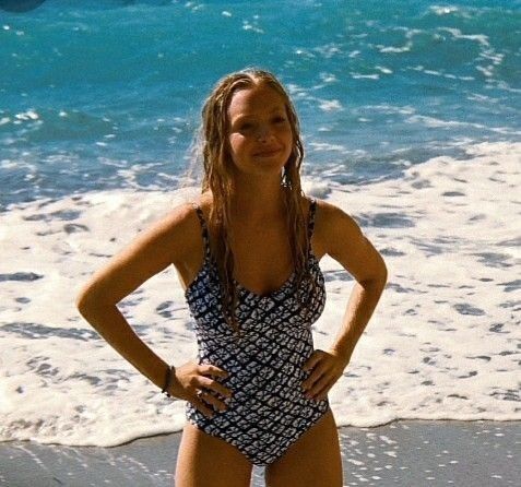 a woman in a swimsuit standing on the beach with her hands on her hips