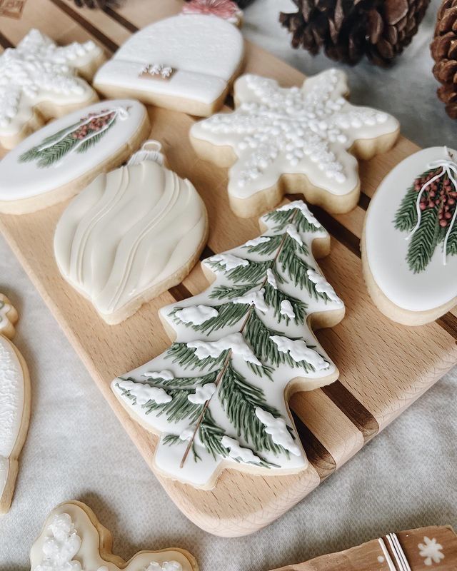 decorated cookies on a cutting board next to pine cones and other holiday decorations, including snowflakes