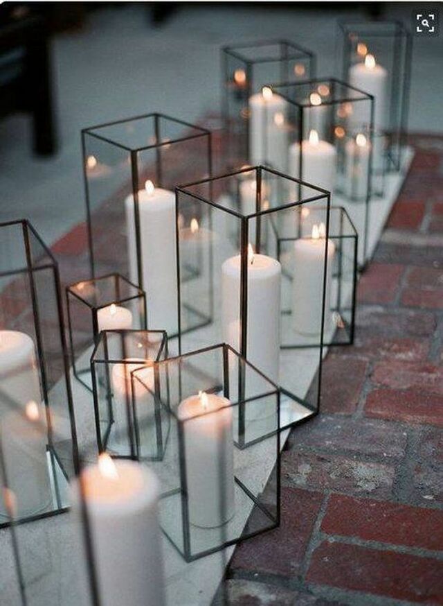 many white candles are placed in glass containers on the brick floor, along with one another