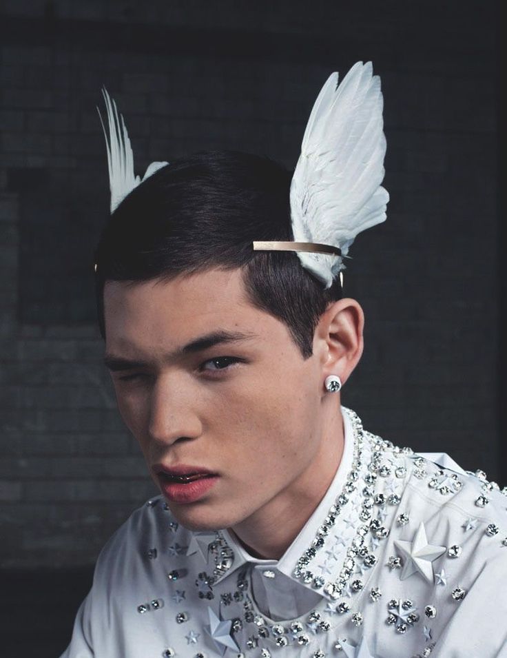 a young man wearing a white shirt with feathers on his head and hair clips in his ears