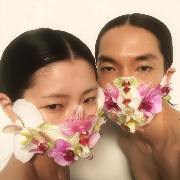 two people with flowers covering their faces in front of the same person's face