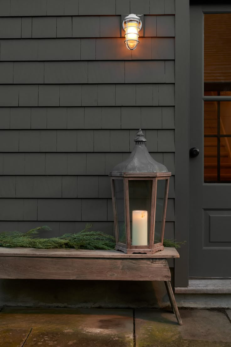 a lit candle sitting on top of a wooden bench in front of a gray house